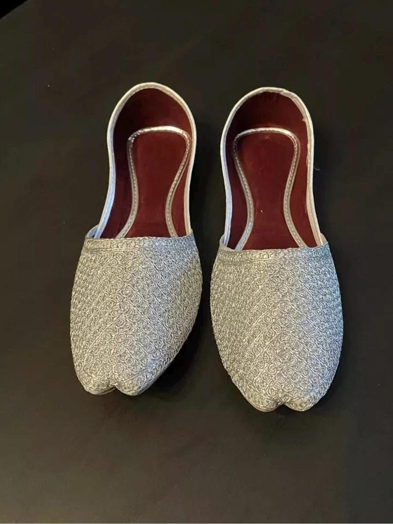 May include: A pair of silver embroidered flat shoes with maroon lining.