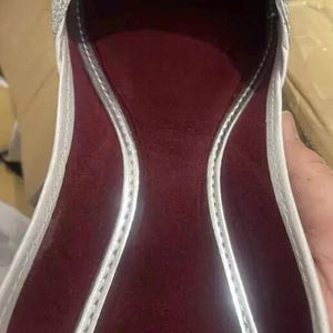 May include: A silver sparkly flat shoe with a burgundy lining. The shoe has a pointed toe and a low heel.