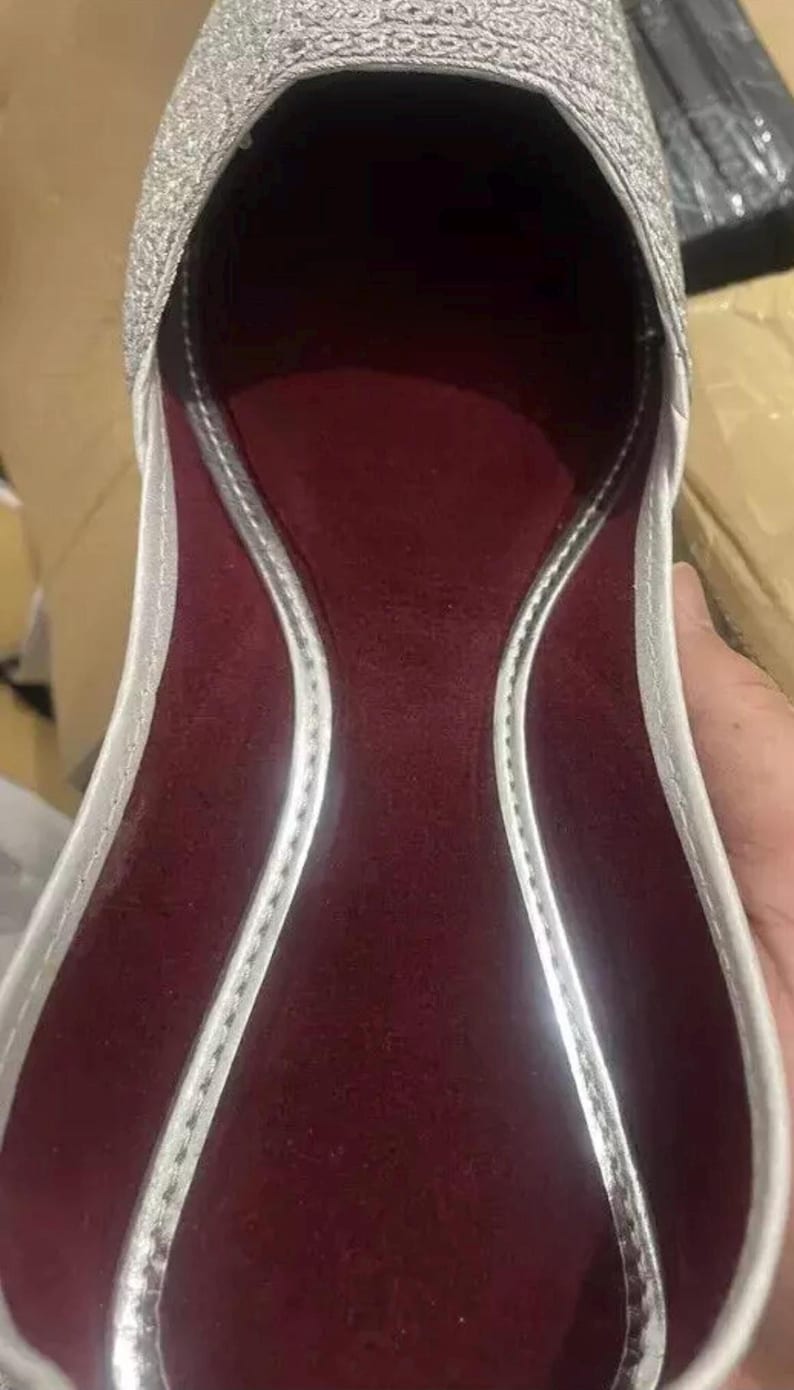 May include: A silver sparkly flat shoe with a burgundy lining. The shoe has a pointed toe and a low heel.
