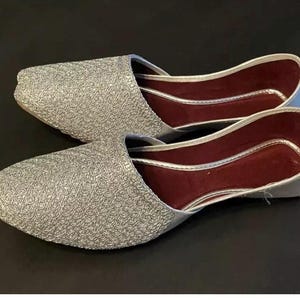 May include: A pair of silver sparkly flat shoes with a burgundy lining. The shoes have a pointed toe and a closed back.
