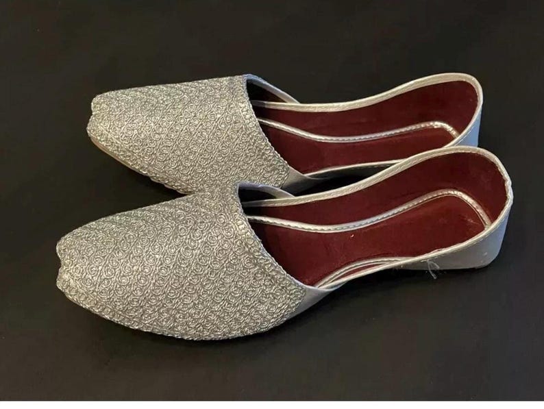 May include: A pair of silver sparkly flat shoes with a burgundy lining. The shoes have a pointed toe and a closed back.
