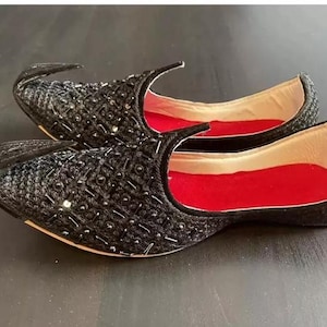 May include: A pair of black embroidered shoes with red lining. The shoes have a pointed toe and a decorative design.