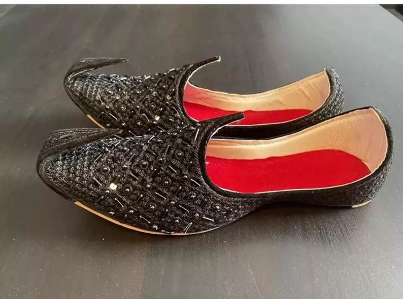 May include: A pair of black embroidered shoes with red lining. The shoes have a pointed toe and a decorative design.