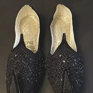 May include: A pair of black embroidered shoes with sequins. The shoes have a pointed toe and a flat sole.