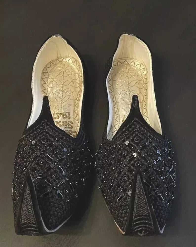 May include: A pair of black embroidered shoes with sequins. The shoes have a pointed toe and a flat sole.