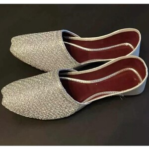 May include: A pair of silver sparkly flat shoes with a burgundy lining. The shoes have a pointed toe and a closed back.