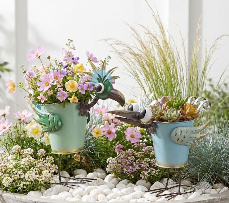 two bird-shaped planters filled with colorful flowers and plants, placed on a bed of rocks.
