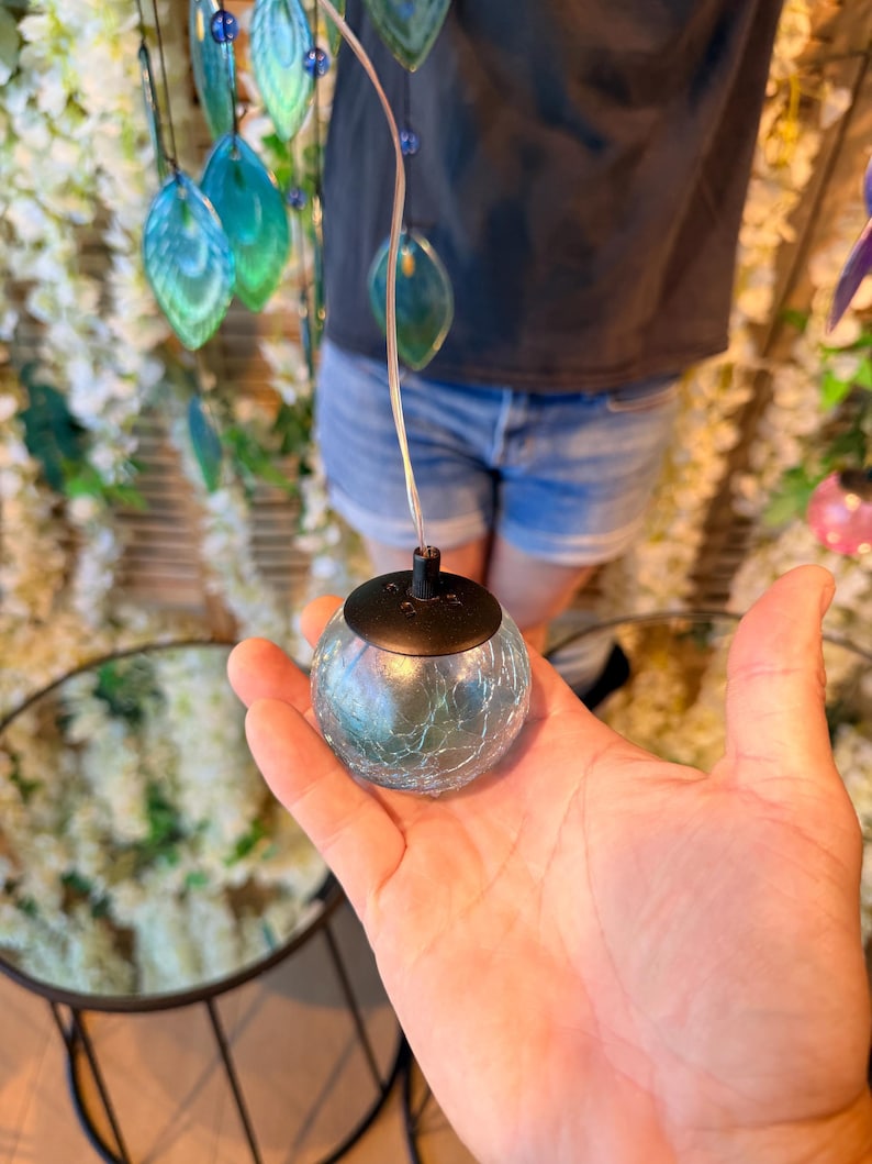 A hand holding a small, round, glass ornament with a black base, against a backdrop of a floral arrangement.