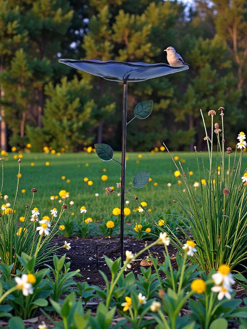 A bird perches on a bird bath in a lush garden filled with yellow flowers and green foliage.