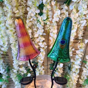 two colorful glass lamps with unique designs, placed on a metal stand in front of a backdrop of white flowers.