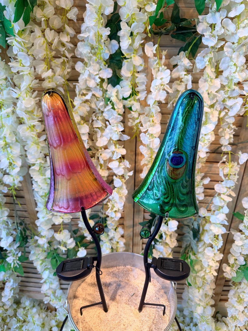two colorful glass lamps with unique designs, placed on a metal stand in front of a backdrop of white flowers.