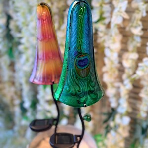 two colorful glass lamps with unique designs, placed on a stand against a backdrop of white flowers.