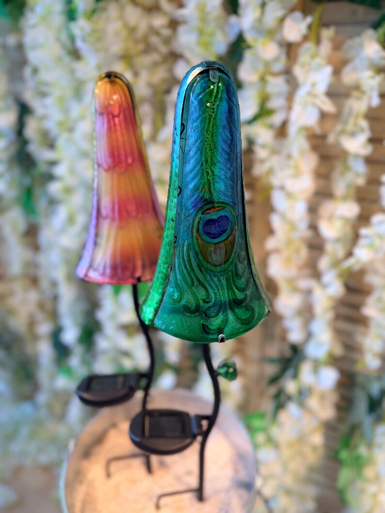 two colorful glass lamps with unique designs, placed on a stand against a backdrop of white flowers.