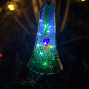 A colorful, illuminated glass ornament resembling a peacock feather is displayed in the image.