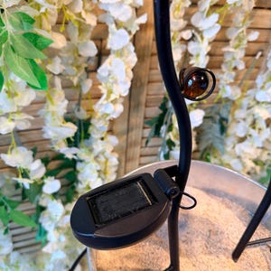 A black metal lamp with a solar panel on the base, placed on a sandy surface.