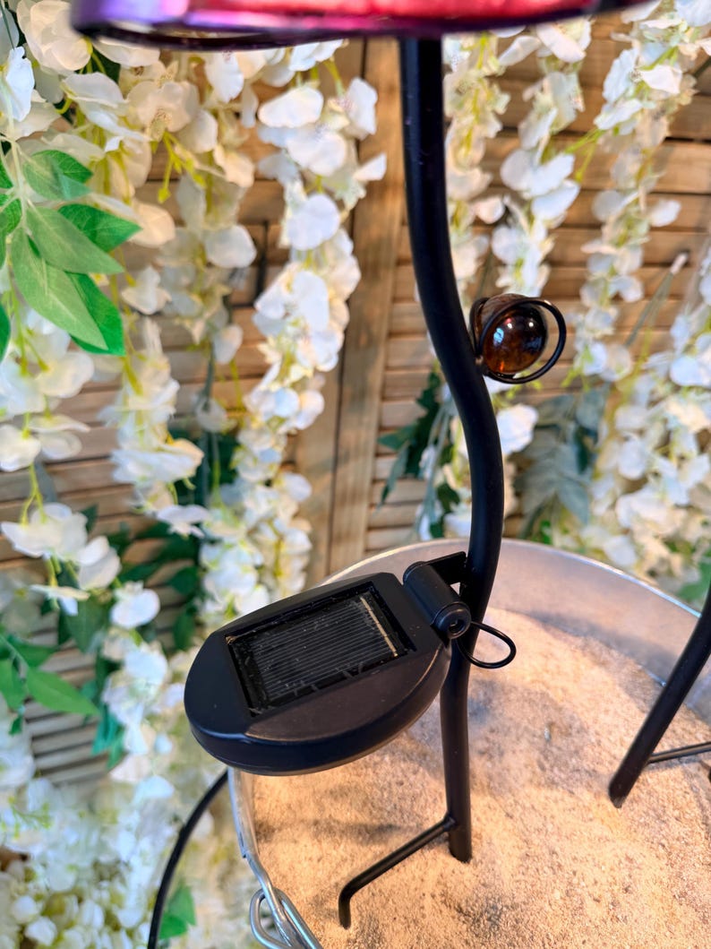 A black metal lamp with a solar panel on the base, placed on a sandy surface.