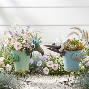 two bird-shaped planters filled with colorful flowers and plants, standing on a bed of small rocks.
