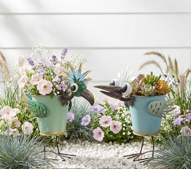 two bird-shaped planters filled with colorful flowers and plants, standing on a bed of small rocks.