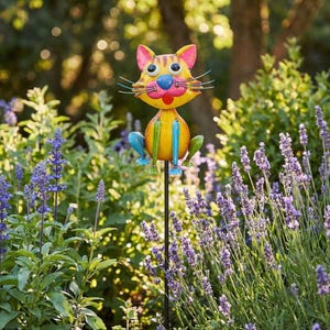 A colorful metal cat figurine is perched on a garden post amidst a lush garden filled with purple flowers.