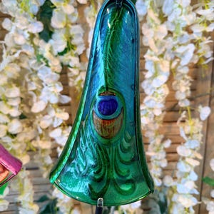 A colorful glass sculpture with a peacock feather design, set against a backdrop of white flowers.