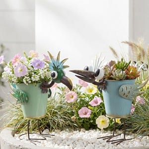 two bird-shaped planters filled with colorful flowers and plants, placed on a bed of white pebbles.