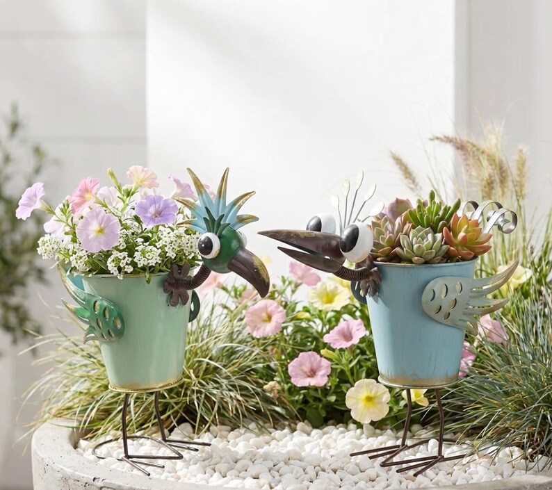 two bird-shaped planters filled with colorful flowers and plants, placed on a bed of white pebbles.