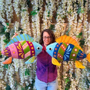 Maceta metálica con forma de pez azul tropical a rayas rosas y moradas para decoración de jardín.