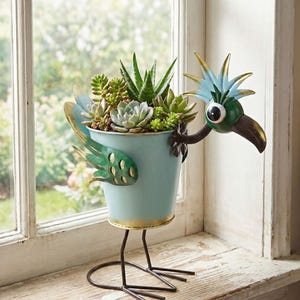 A bird-shaped planter filled with a variety of succulent plants and other greenery, placed on a windowsill.
