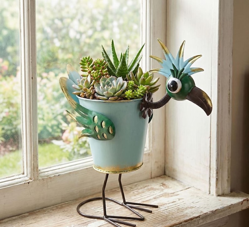 A bird-shaped planter filled with a variety of succulent plants and other greenery, placed on a windowsill.