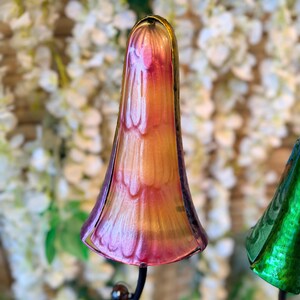 A colorful glass sculpture resembling a flower or plant stands in the foreground, with a blurred background of white flowers.