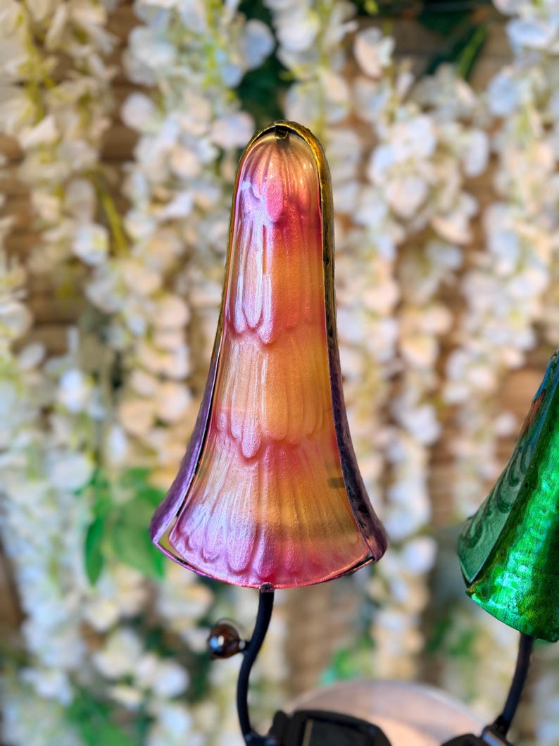 A colorful glass sculpture resembling a flower or plant stands in the foreground, with a blurred background of white flowers.