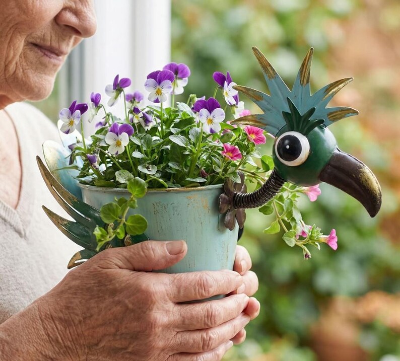 An elderly woman holds a blue pot filled with purple and white flowers, which are decorated with a bird-like metal sculpture.