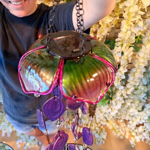 A person is holding a colorful glass wind chime with purple and green glass pieces hanging from it.
