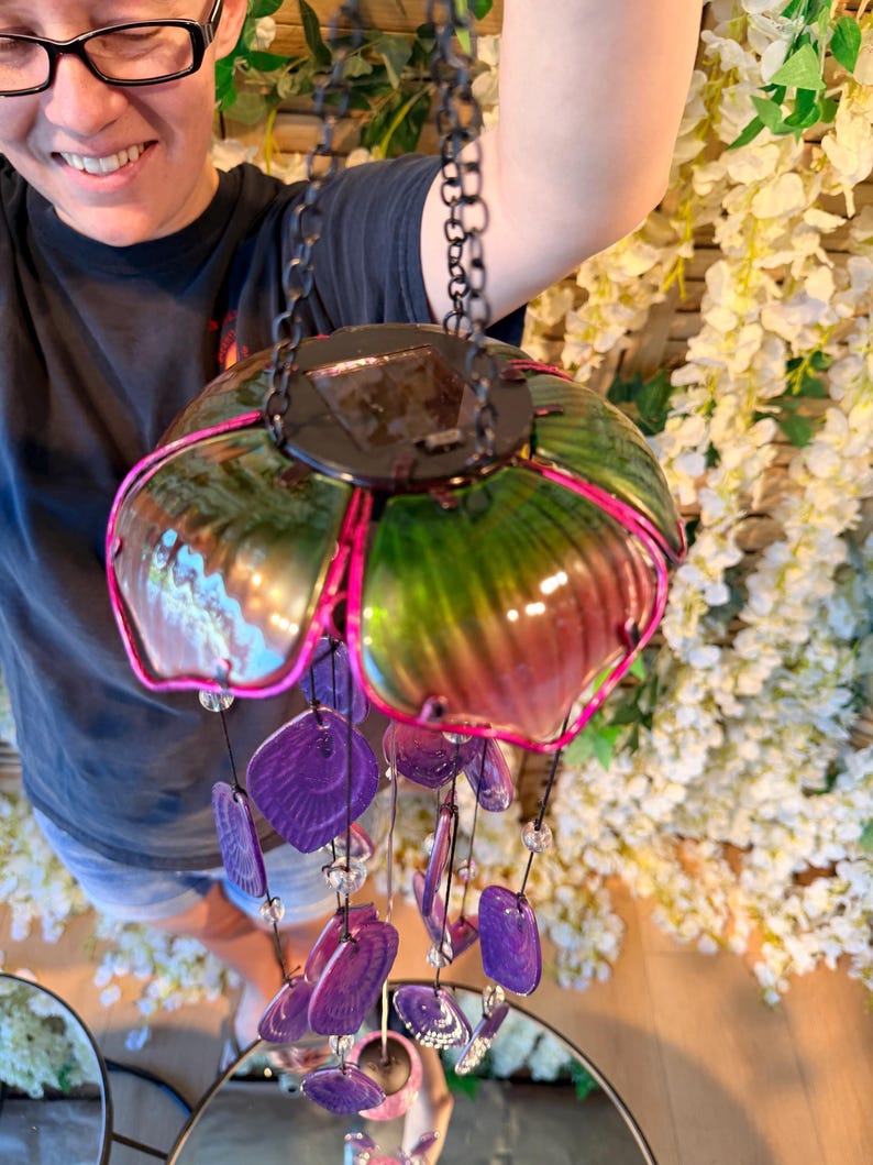 A person is holding a colorful glass wind chime with purple and green glass pieces hanging from it.