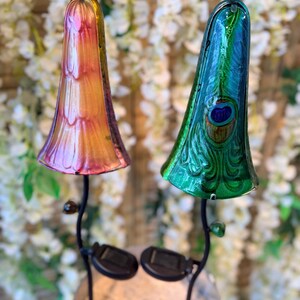 two colorful glass lamps with unique designs, placed on a stand against a backdrop of white flowers.