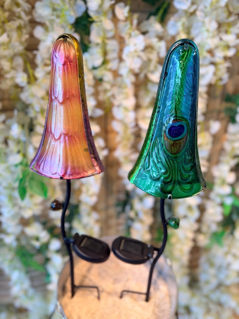 two colorful glass lamps with unique designs, placed on a stand against a backdrop of white flowers.