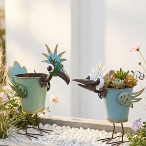 Two metal bird-shaped planters filled with colorful succulent plants, placed on a bed of white pebbles.