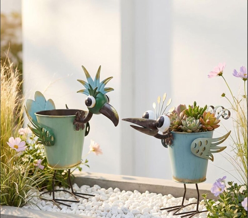 Two metal bird-shaped planters filled with colorful succulent plants, placed on a bed of white pebbles.