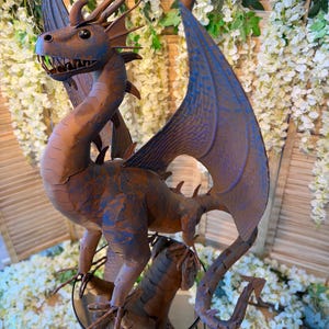 A large metal dragon statue with a dragon head and wings, sitting on a stand surrounded by white flowers.