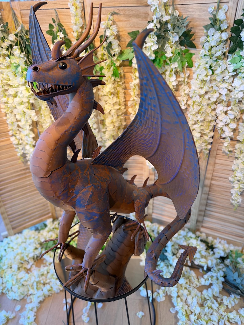 A large metal dragon statue with a dragon head and wings, sitting on a stand surrounded by white flowers.