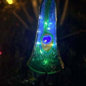 A colorful glass ornament with a blue and green pattern, illuminated by small lights, is displayed in a dark outdoor setting.
