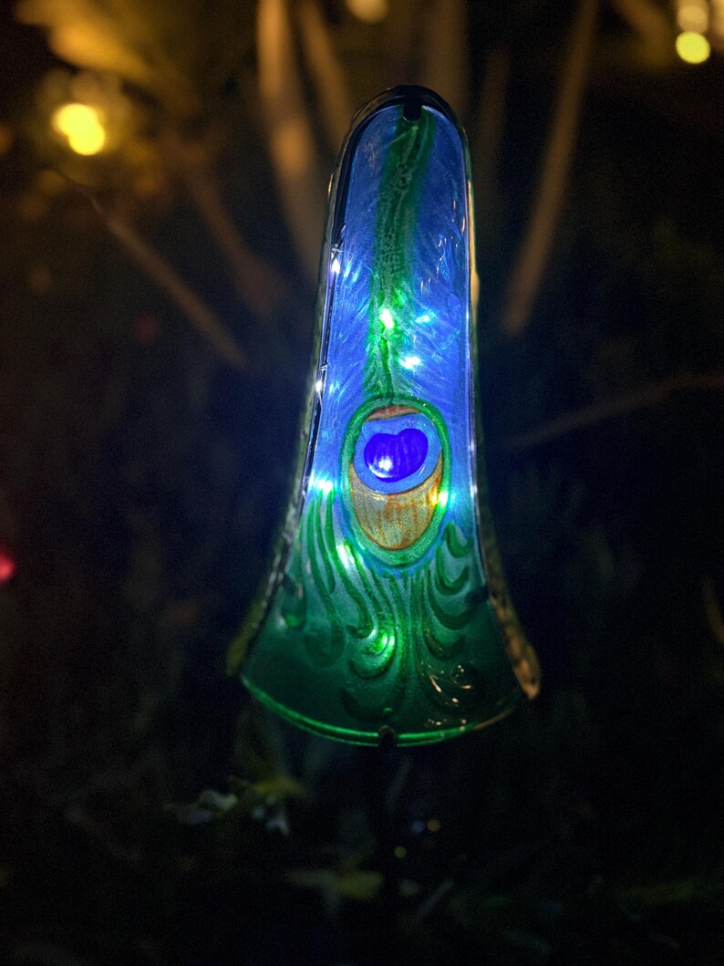 A colorful glass ornament with a blue and green pattern, illuminated by small lights, is displayed in a dark outdoor setting.