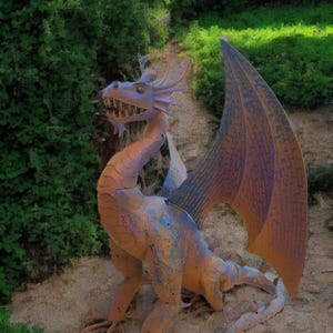 A colorful dragon statue stands on a dirt path surrounded by lush greenery.