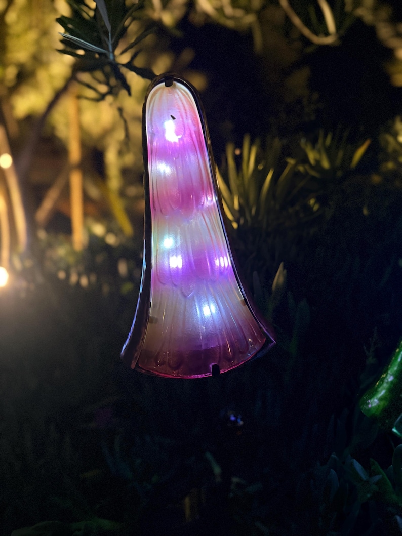 A colorful, illuminated object resembling a flower or mushroom is hanging from a branch in a dark, natural setting.