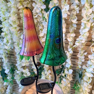 two colorful glass lamps with unique designs, placed on a stand in front of a backdrop of white flowers.