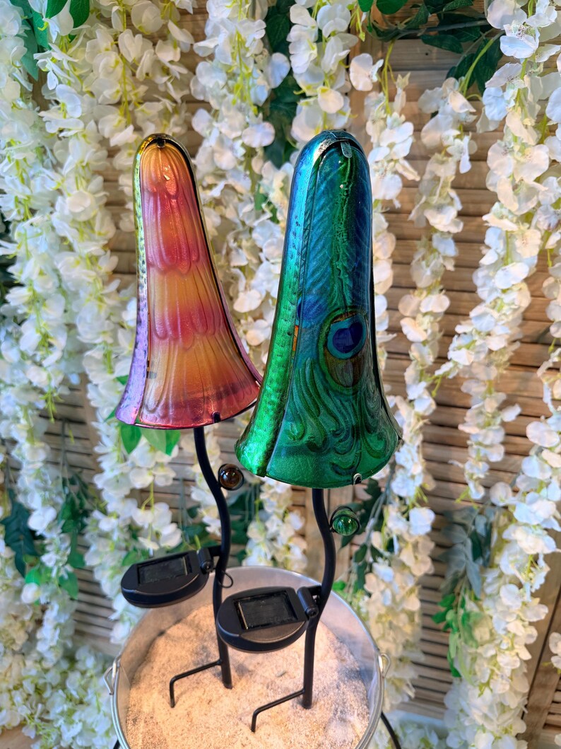 two colorful glass lamps with unique designs, placed on a stand in front of a backdrop of white flowers.