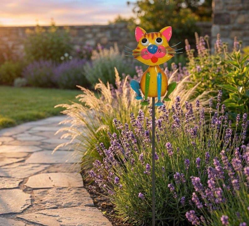 A colorful garden ornament resembling a cat is placed on a stone path surrounded by purple flowers and greenery.