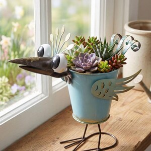 A blue metal bird-shaped planter filled with a variety of colorful succulent plants and flowers, placed on a wooden surface near a window.