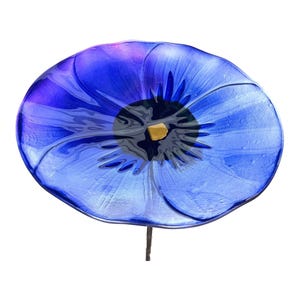 A large, vibrant blue glass flower with a yellow center is the central focus of the image.