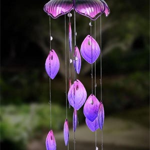 A solar-lit glass peacock tail wind chime with a variety of purple and pink feathers hanging from it.